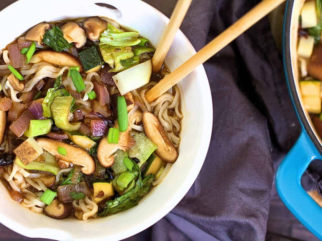 Bowl of noodles with vegetables and mushrooms, served with chopsticks.