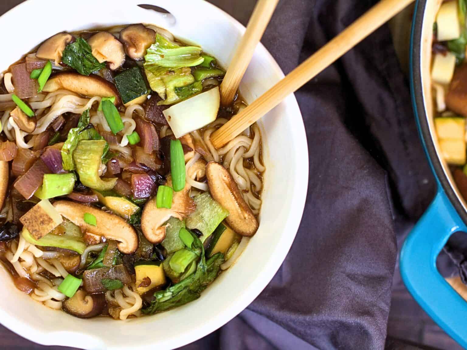 Bowl of noodles with vegetables and mushrooms, served with chopsticks.