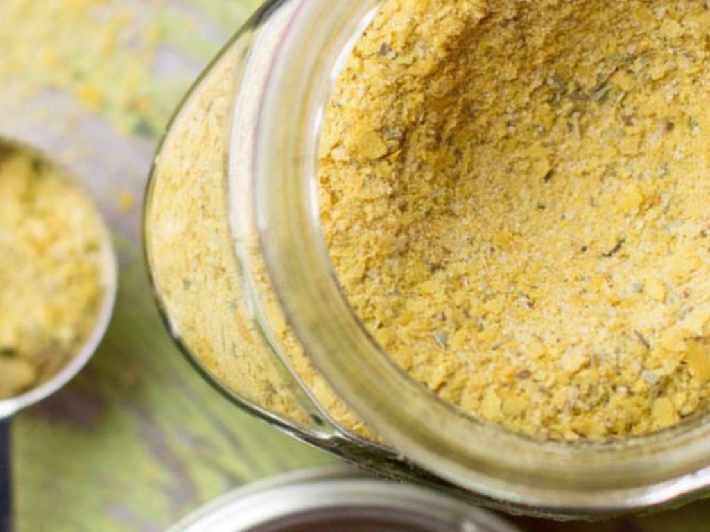 Jar of vegan chicken broth powder with a spoonful on a green surface