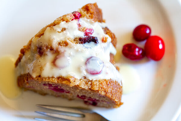 Slice of cake with dairy free cream and cranberries on a white plate