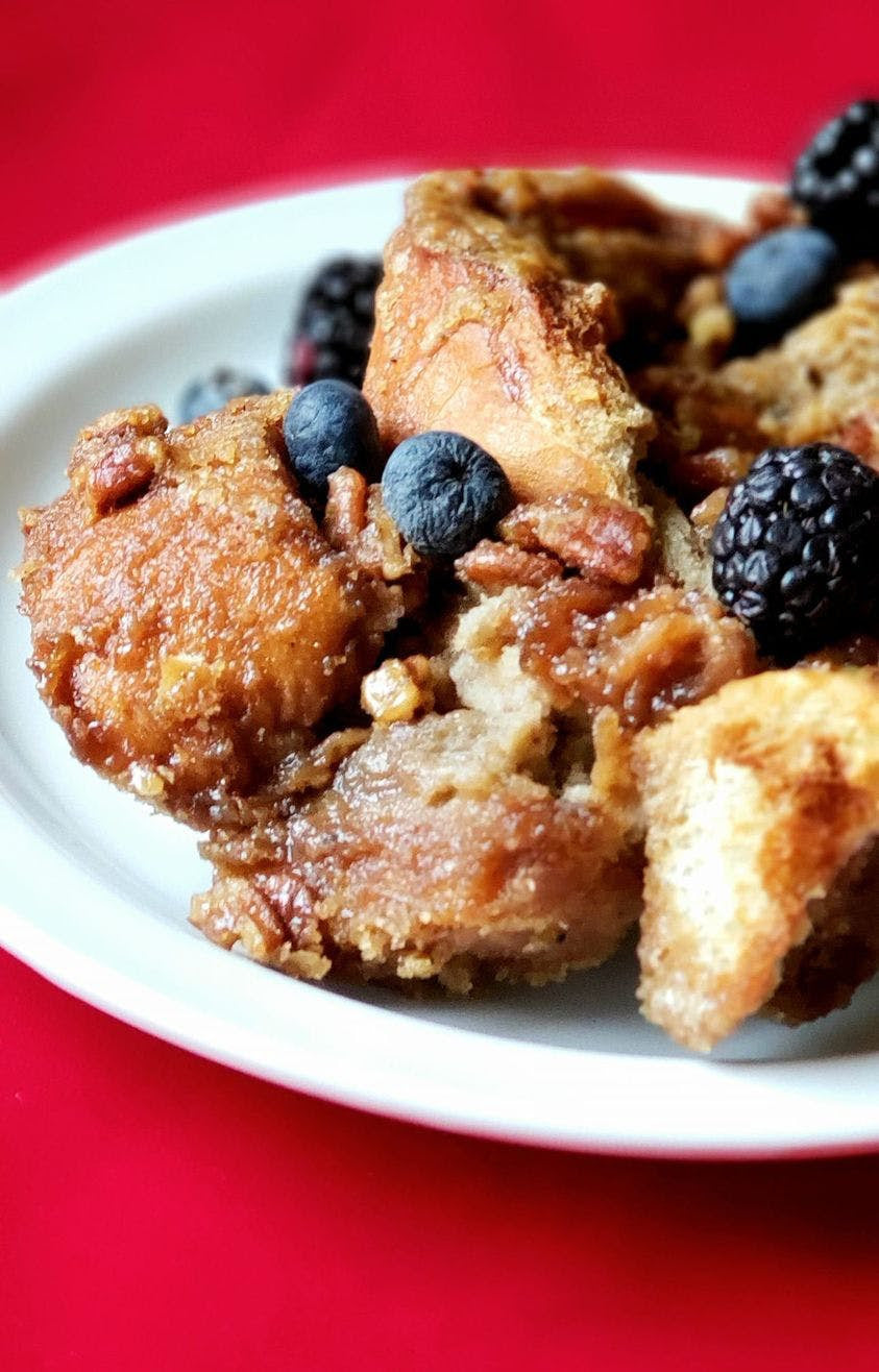 French toast casserole with blueberries and blackberries on a white plate against a red background