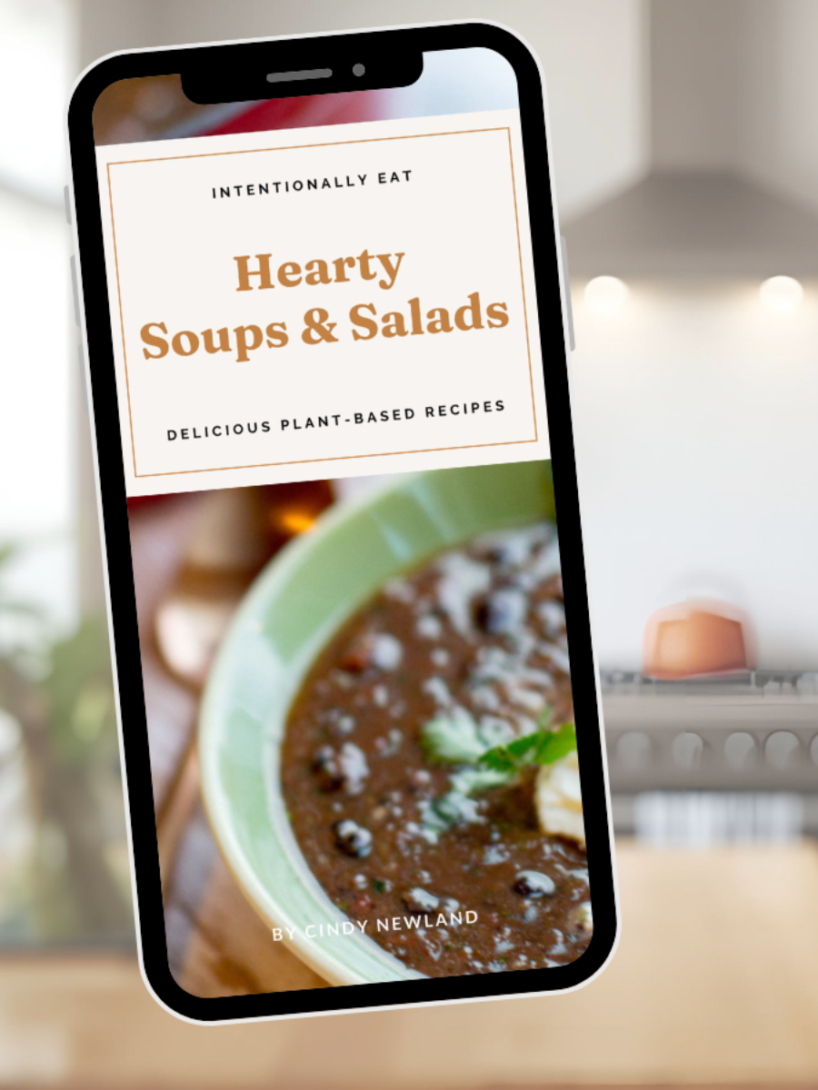 Phone displaying a recipe book cover for 'Hearty Soups & Salads' with a blurred kitchen background.