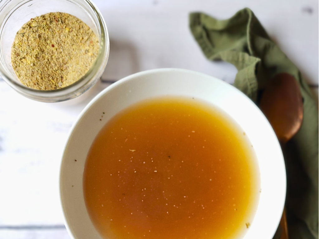 Bowl of broth with a jar of seasoning and cloth on a white surface
