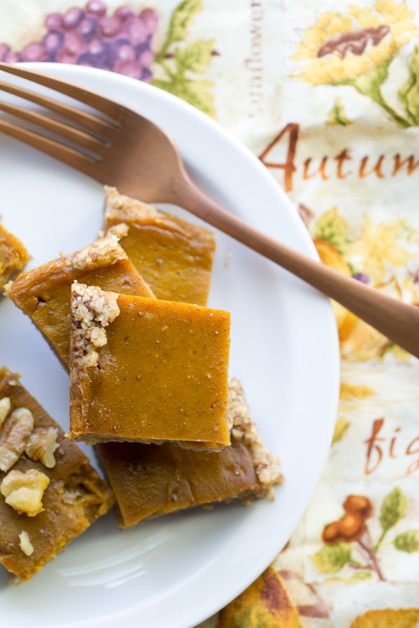 Pumpkin bars on a plate with a fork, placed on an autumn-themed tablecloth.