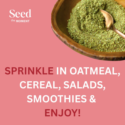 Green powder in a bowl with a spoon on a pink background, featuring 'Seed the Moment' brand.