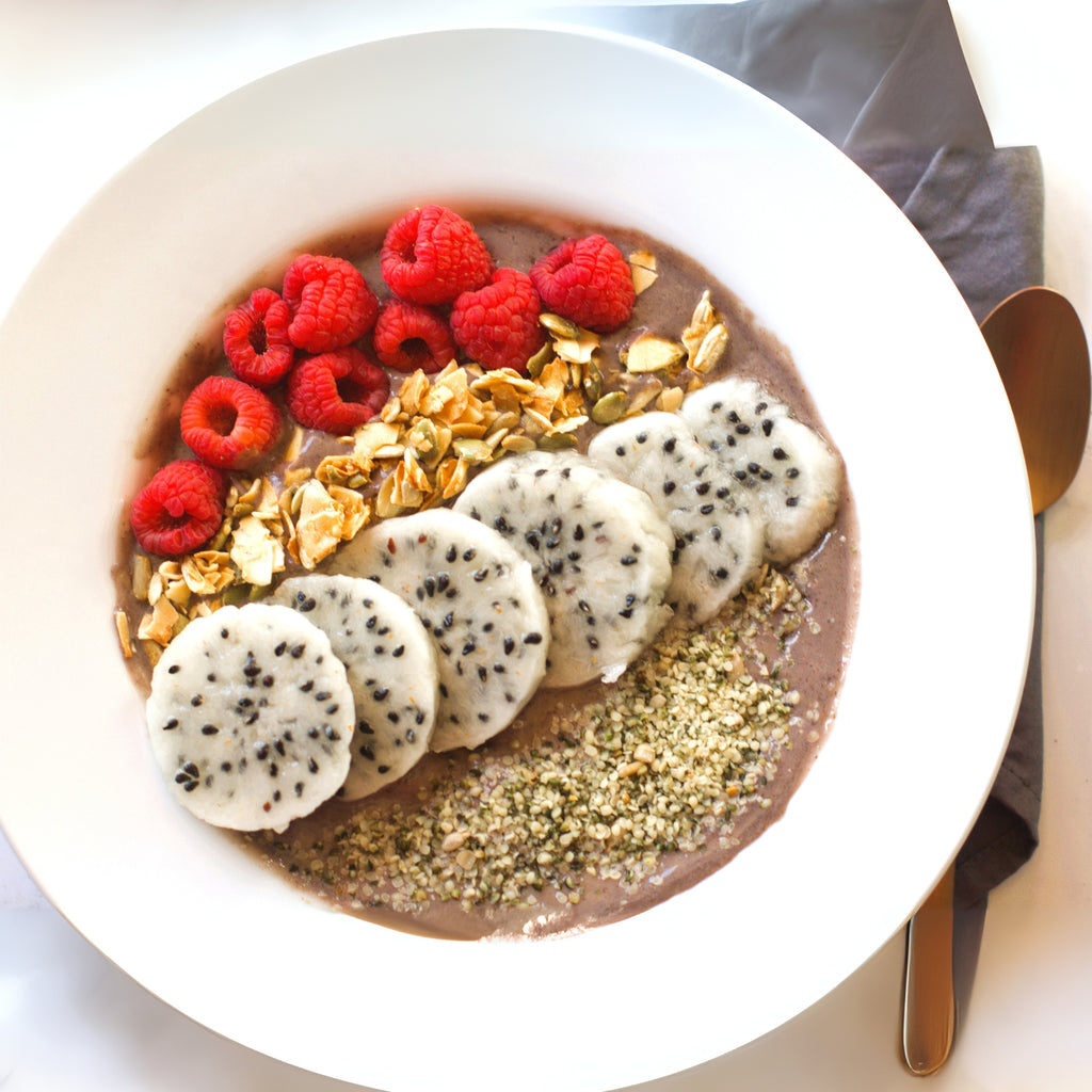 Fruit and granola bowl on a white plate with a spoon on the side.