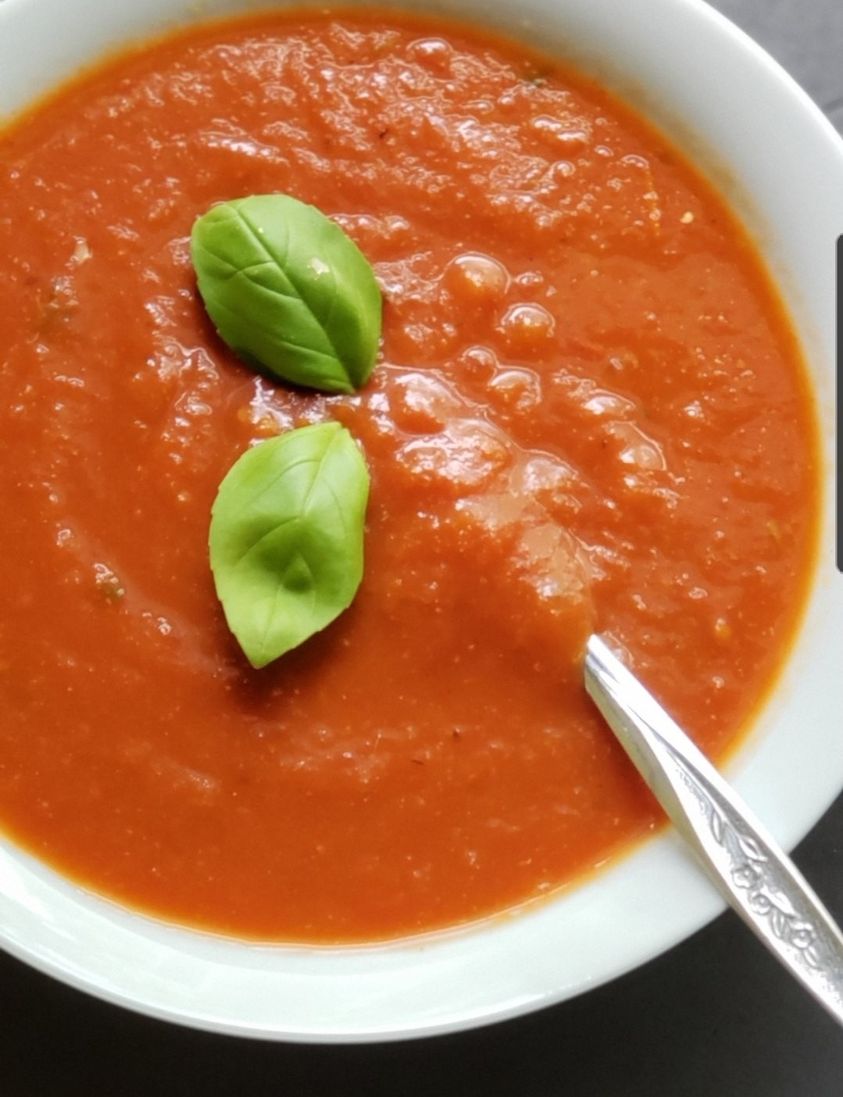 Tomato soup with basil leaves in a white bowl on a dark background