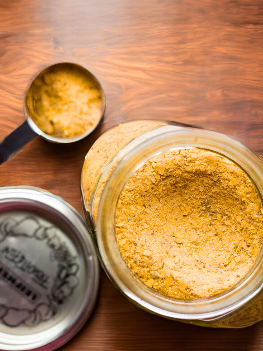 Open jar of vegetable bouillon powder with a measuring spoon on a wooden surface